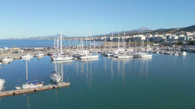 Aerial view of Rethymno marina in Crete with luxury yachts and fishing boats moored in the turquoise mediterranean sea along the historic coast