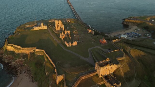 Sunset casts a warm glow over Tynemouth Pier along the North Sea at dusk drone flyover