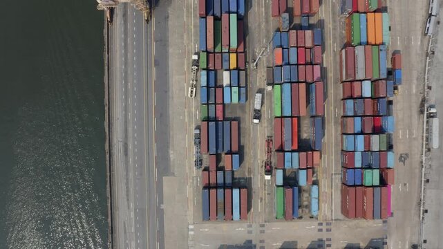 A dynamic aerial time-lapse of a bustling port, where cranes load massive container ships under a dramatic, time-compressed sky.

