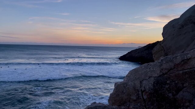 Surfers paddle beneath dramatic cliffs at sunset near Zavial Beach, where Atlantic waves and fading light define the raw energy of the Algarve coast