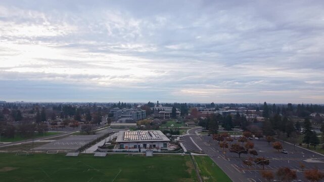 Panning drone view above California State Stanislaus University, with soft cloud cover muting the sky below the campus.
