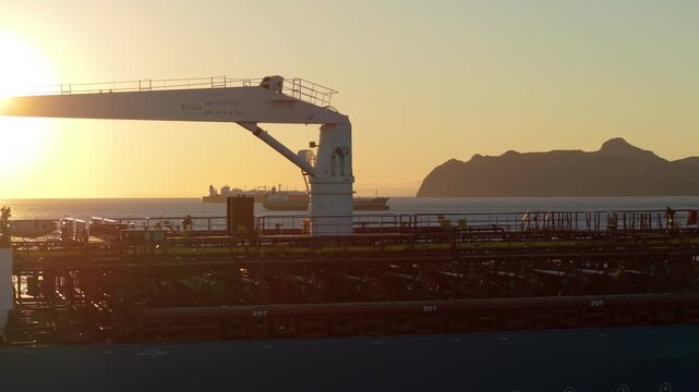 Aerial close-up of tanker deck flying sideways at sunset. Maritime cargo vessel with visible equipment and two ships in the distance. Industrial, shipping and global trade theme.