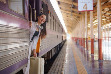 Obraz premium A cute Asian traveler woman carrying a suitcase is waiting for the train at the train station.