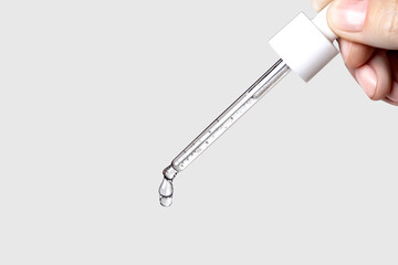 Obraz premium Pipette with serum in hand. Drips drop isolated on gray background, copy space photo close up