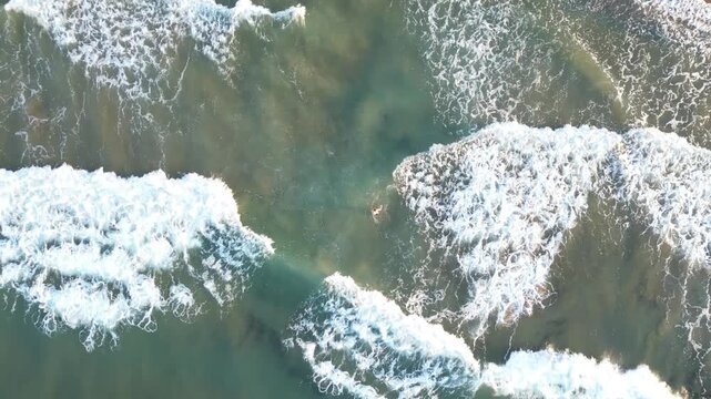 Top-down drone view of a woman swimming in Crete&rsquo;s stormy seas, surrounded by swirling foam and deep sapphire waves, capturing raw Mediterranean power. Travel in Greece
