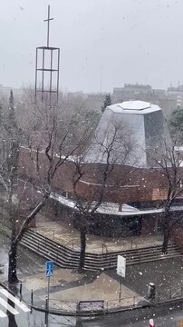 Nevando copos de nieve en calle de ciudad con fr&iacute;o, iglesia con parroquia, cruz religiosa y autob&uacute;s