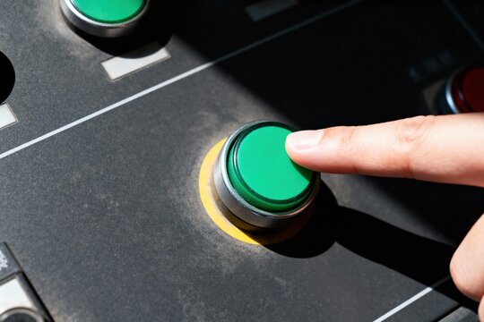 Close-up of hand pressing green button on control panel.