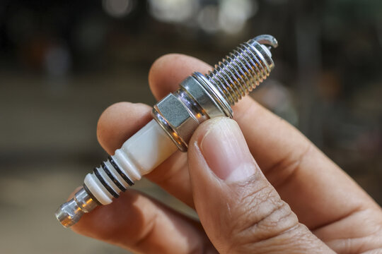 Focused mechanic hand holding new spark plug. An essential engine part for automotive repair and vehicle maintenance, crucial for ignition system service in garage