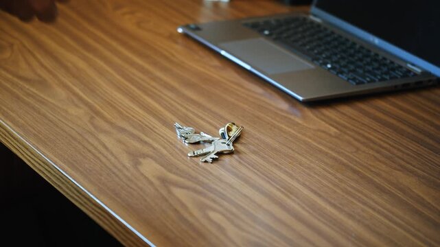 A close-up shot of a set of metal keys being placed onto a wooden table surface. The keys make contact with the wood and settle naturally into a small pile, producing clean, crisp metallic key sounds