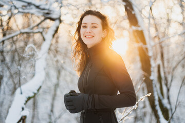 Cheerful woman in ski suit and gloves smiling at camera in winter forest 