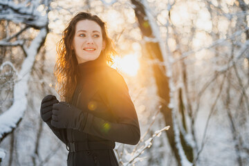 Cheerful woman in gloves and ski suit standing in forest during sunset 