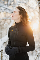 Portrait of woman in ski suit and gloves posing in winter forest during sunset 