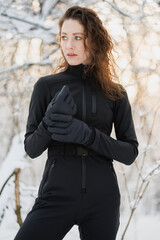 Portrait of brunette woman in ski suit and gloves posing in forest at sunset 