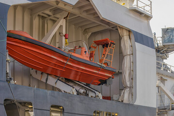 bright orange rigid inflatable boat is lowered from a ship's deck using a mechanical davit, ready for emergency deployment at sea