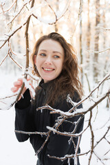 Positive brunette woman in ski suit standing near tree branches in winter forest 