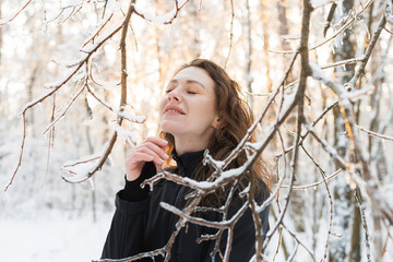 Joyful woman in ski suit standing near tree branches with snow in forest 