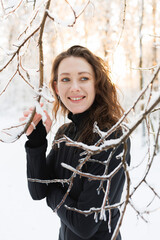 Happy woman in ski suit standing near tree with snow in winter forest 