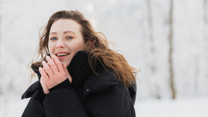Positive woman warming hands and smiling at camera in winter forest 