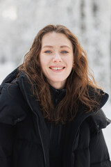 Cheerful brunette woman in outerwear looking at camera in winter forest 