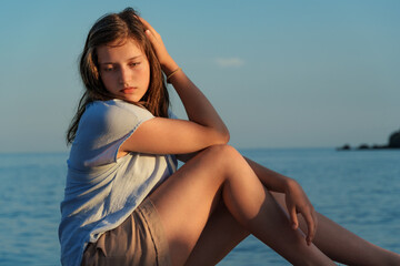 Naklejka premium Close up portrait of a pensive young woman touching her hair at sunset on the Adriatic coast in Montenegro.