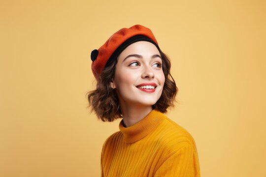 Young woman smiling with an orange beret and yellow sweater on a yellow background