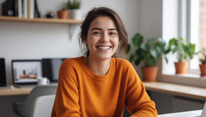 Cheerful young female freelancer looking at camera and smiling while sitting at workplace in office