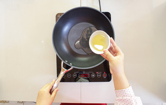Person pouring cooking oil into a hot frying pan on induction stove