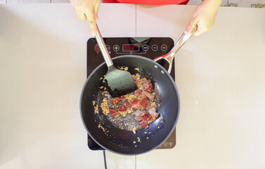 Asian woman cooking beef and garlic on induction stove in kitchen