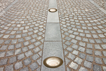 New paving made with grey stone slabs and small stone cube blocks interlocked with sand in curved shape in a pedestrian zone with recessed floor lamp © Francesco Scatena