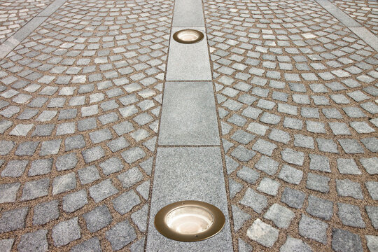 New paving made with grey stone slabs and small stone cube blocks interlocked with sand in curved shape in a pedestrian zone with recessed floor lamp