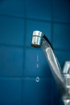 Leaking faucet drips water against blue tiled wall