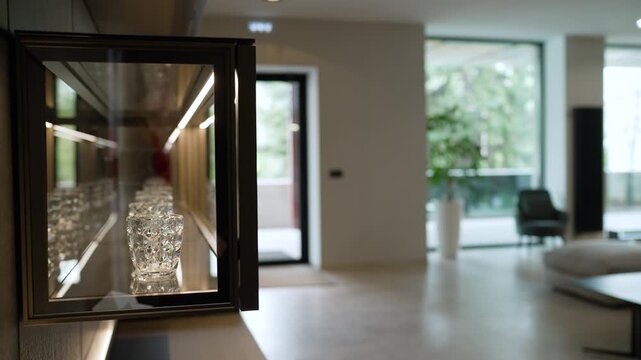 Elegant crystal drinking glasses neatly arranged on a reflective shelf inside a modern, illuminated display case. The camera slowly pulls back
