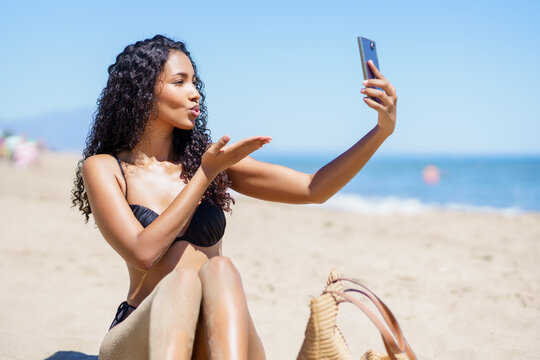 A Young Woman Happily Taking a Selfie on the Beach While Dressed in a Stylish Bikini