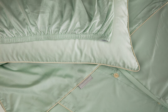 A silk bedding set is laid out on a flat surface. The set includes a duvet cover and pillowcases in soft green color. The fabric appears smooth and shiny, showing a clean and neat arrangement.