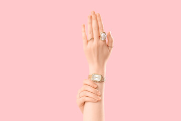 Female hands in golden wrist watch and beautiful rings on pink background