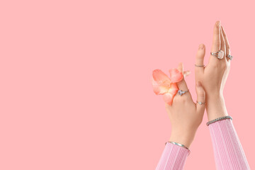 Female hands in silver bracelets and rings with beautiful flower on pink background