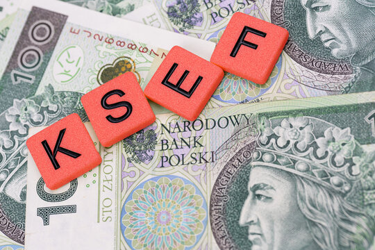 Blocks with the abbreviation KSEF, standing for National E-invoice System, are placed against a background of loosely spread Polish 100 PLN banknotes. The photo was taken under artificial lighting.