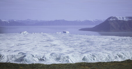 Vast ice formations stretch across the foreground, leading to a tranquil ocean. Majestic mountains rise in the distance under a clear sky, showcasing the beauty of nature in winter.