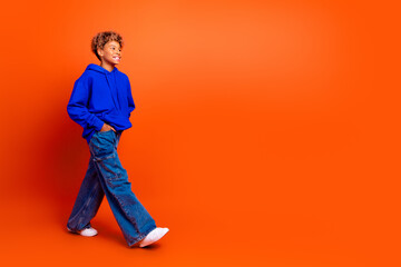 Naklejka premium Young boy in blue hoodie walking on orange background smiling and showing casual fashion lifestyle stock image