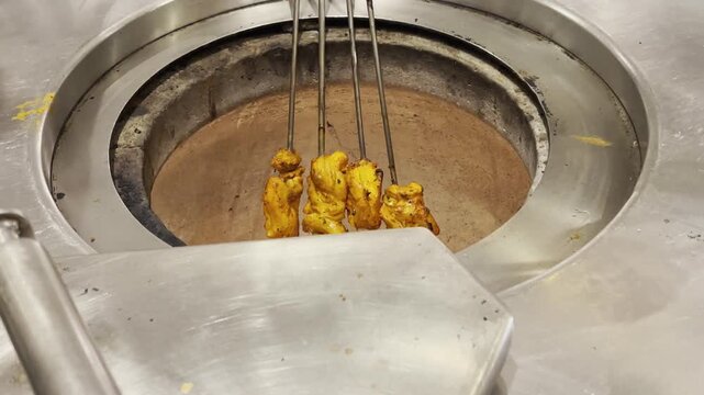 Close-up of marinated chicken skewers grilling over an open flame in a traditional tandoor-style oven. Juicy orange-spiced chicken cooks on metal skewers, sizzling with heat and smoke. Perfect for foo