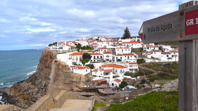 Panoramic view from iconic Azenhas do Mar viewpoint with a trail sign, white cliffside seaside houses and the Atlantic Ocean below in daylight. Traditional Portuguese coastal village on the cliffs