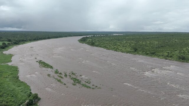 Smooth aerial drone footage descending over a flooded river in Kruger National Park, South Africa, showing high water levels and natural bush veld savanna.