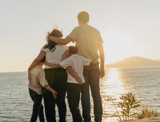 Young family with two sons hugging and watching sunset at the sea, travel and togetherness concept