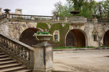Obraz premium Spring scene in a historic European garden with stone architecture, arches, and stairs. A decorative stone planter filled with blooming tulips stands in the foreground