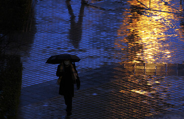 Reflejos de luz dorada con destello en d&iacute;a de lluvia con silueta de persona con paraguas bajo la lluvia