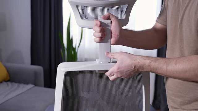 Man installing adjustable headrest on mesh ergonomic office chair. Close up of furniture assembly at home, modern workspace, unbranded office furniture.