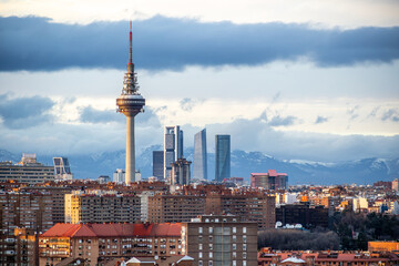 Obraz premium Urban landscape of Madrid with TV tower, residential roofs, green winter trees and modern skyline on the horizon.