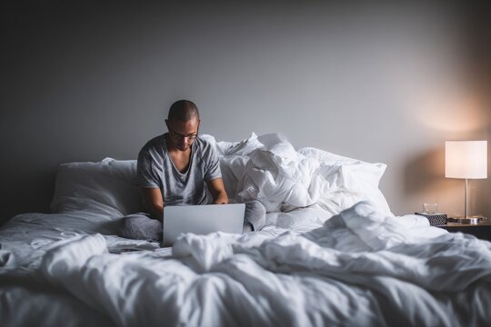 Man using laptop in bed with rumpled white sheets