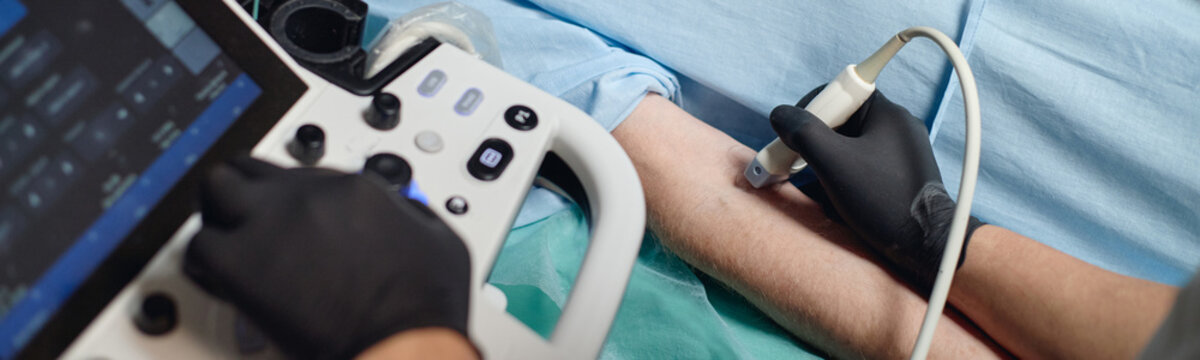 Website header shot of Caucasian adult arm undergoing vascular ultrasound examination by gloved medical professional using diagnostic ultrasound device in clinical vascular center setting