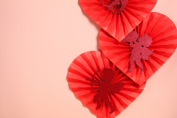 Red paper hearts with glitter cupids arranged on pink background with copy space